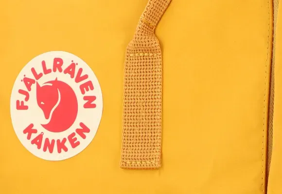 Närbild av logotyp och rem på gul Kanken-ryggsäck